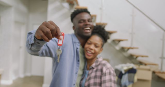 Image of happy african american couple embracing, showing keys to new house. love, relationship, and starting new life together.