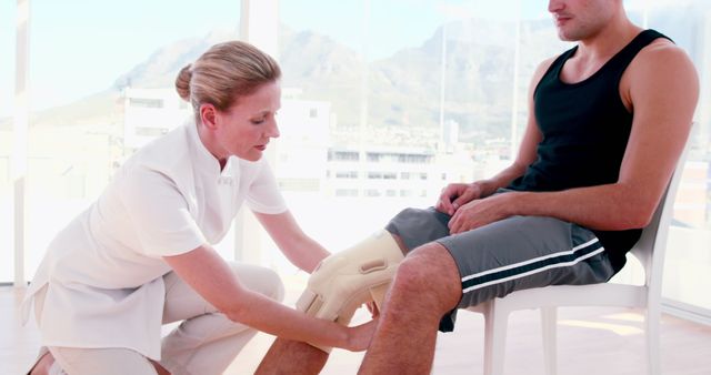 Physical therapist applying a knee brace to a patient during rehabilitation. The patient is wearing casual athletic clothing, while the therapist, in a white uniform, is providing medical care. Suitable for use in health and wellness articles, sports injury recovery guides, medical blogs, physical therapy websites, and orthopedic clinic promotional materials.