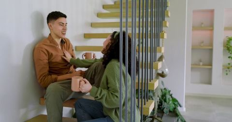 Happy Mixed Couple Chatting on Modern Staircase with Coffee