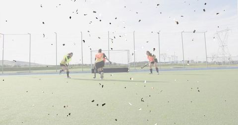 Women practicing field hockey goal drill on synthetic turf with scattered debris