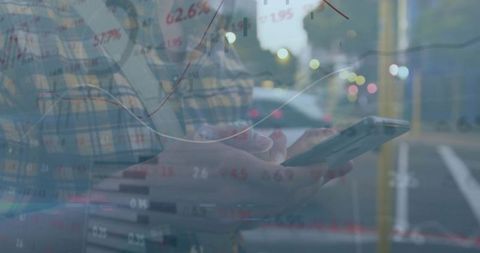 Man checking smartphone while financial market charts overlay city street at dusk