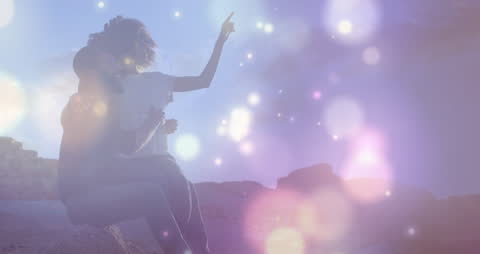 Romantic Couple Enjoying Sunset on Rocks with Sparkling Lights