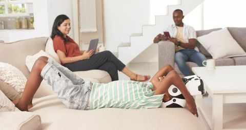 Teen using virtual reality headset while parents relax with devices in living room