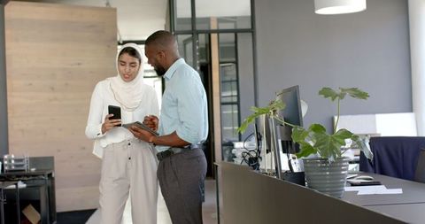 Professional colleagues discussing work on digital devices in modern office