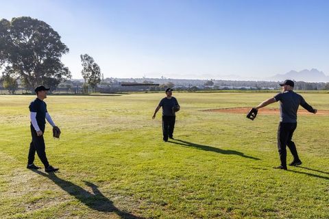 Three Adults Practicing Baseball Fielding Drill on Sunny Outfield with Long Shadows