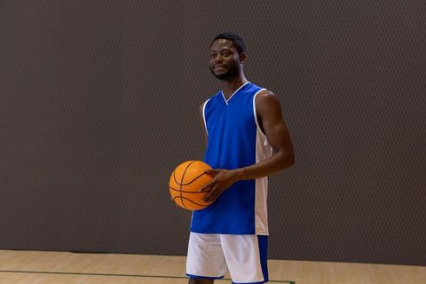African american basketball player holding ball on hardwood court wearing blue jersey