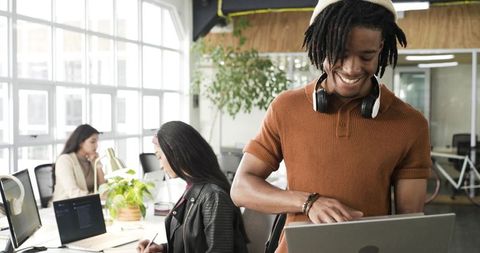 Young professionals collaborating in sunlit coworking space with laptop and headphones
