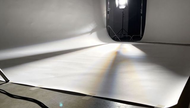 Empty white seamless cyclorama with studio lights, paper backdrop, cables and tape