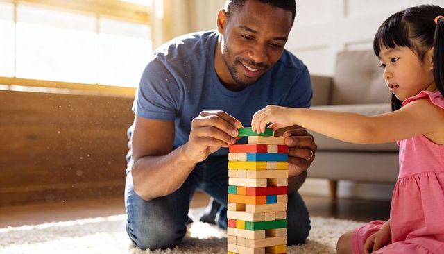 Caregiver guiding child building colorful wooden block tower in sunlit living room