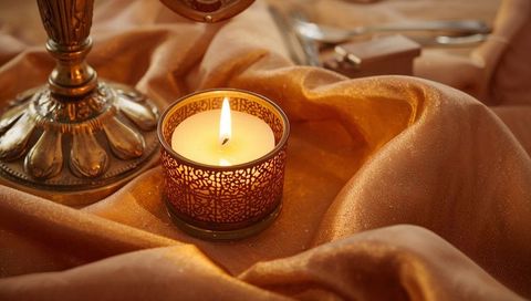 Filigree votive candle casting warm lacy glow over bronze satin fabric for cozy ambience