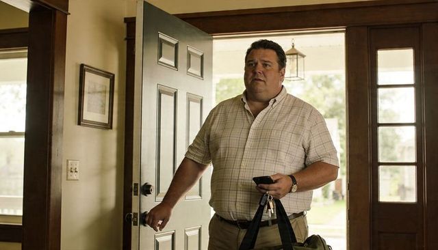 Middle-aged man arriving home carrying duffel bag and keys while holding smartphone