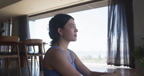 Serene woman sitting by large window looking out at coastal city skyline