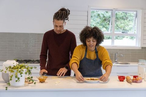 Diverse couple baking together in bright kitchen preparing pie dough and filling