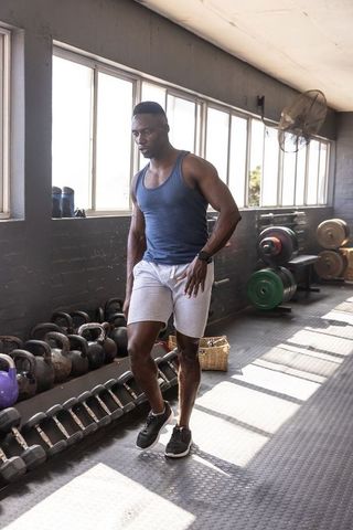 African american man training in sunlit gym with kettlebells, weight plates, athletic wear