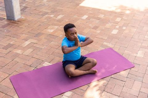 African american boy practicing outdoor yoga on purple mat meditating cross-legged