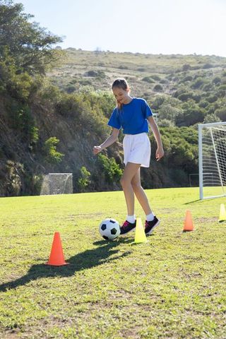 Teenage girl practicing soccer dribbling on field