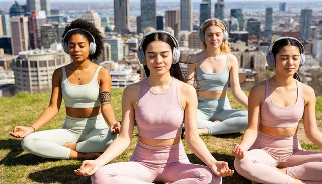 Diverse women meditating with headphones on urban hill overlooking city skyline