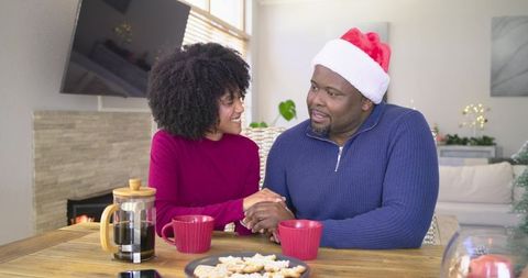 African American couple sharing cozy holiday moment with coffee and cookies by fireplace