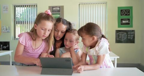 Multicultural girls collaborating on tablet in classroom, digital learning and teamwork