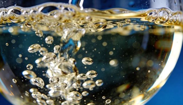 Golden champagne bubbles rising in stemmed glass closeup macro with sparkling bokeh