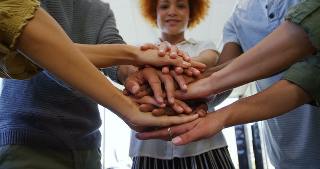 Diverse group of colleagues stacking hands together in a display of unity and teamwork in a modern office environment. Perfect for use in corporate materials, team building activities, motivational campaigns, and business presentations.