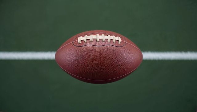 American football hovering over field turf with yard line