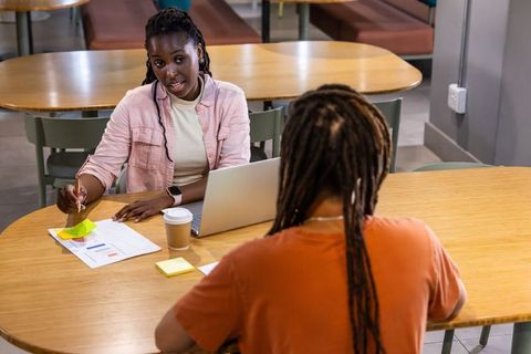 African american women collaborating over laptop and charts in modern cafeteria meeting