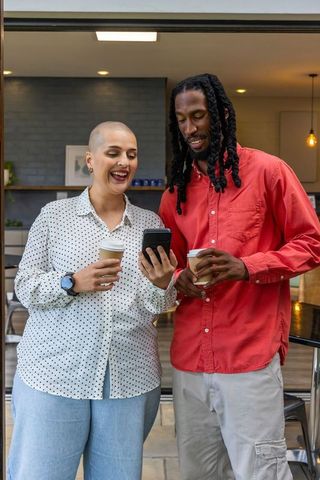 Friends sharing coffee and smartphone, smiling and chatting in modern kitchen doorway