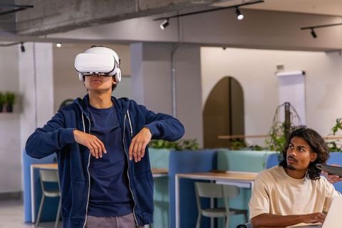 Diverse male coworker testing vr headset while colleague watching in coworking space