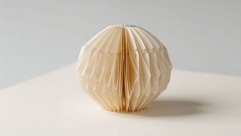 Cream paper honeycomb ball sitting on pale tabletop minimalist decorative ornament