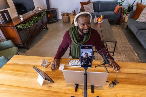 African american man recording livestream at cozy home office with microphone and phone