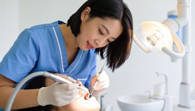 Female dentist performing oral exam and cleaning using mirror and suction under lamp