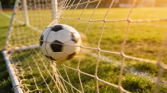 Soccer ball hitting net at sunset capturing goal moment with motion blur and lens flare