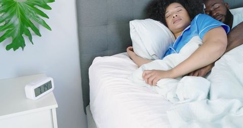 African american couple sleeping and embracing in cozy morning bed with alarm clock