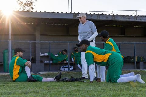 Baseball coach guiding players in dugout at sunset with warm lens flare