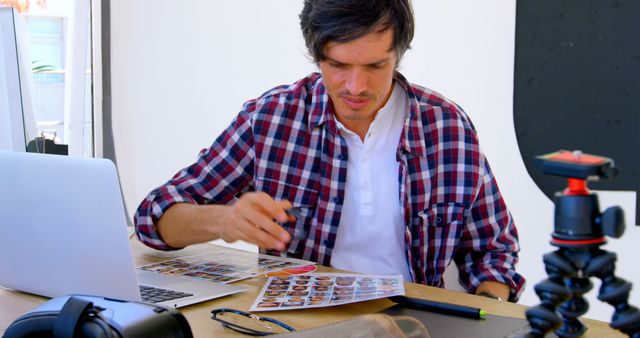 Caucasian man reviews photos at a home office desk. His workspace is equipped for photo editing and camera gear maintenance.