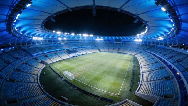 Empty modern soccer stadium under blue led floodlights with pristine pitch and scoreboard