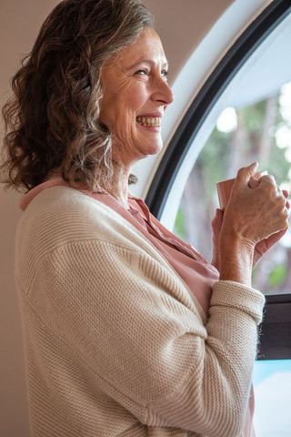 Senior woman enjoying coffee standing by arched window