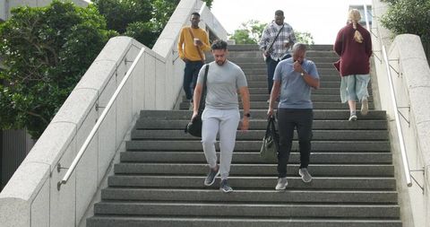 Commuters descending concrete stairs carrying duffel bags in urban overcast commute