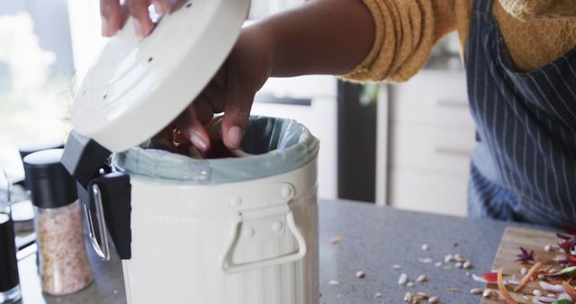 Person opening the lid and placing food waste in kitchen compost bin. Concept of waste reduction and maintaining a clean home environment. Ideal for content on eco-friendly practices, kitchen tips, and home sustainability. Perfect for articles or advertisements promoting composting, recycling, and environmentally conscious living.