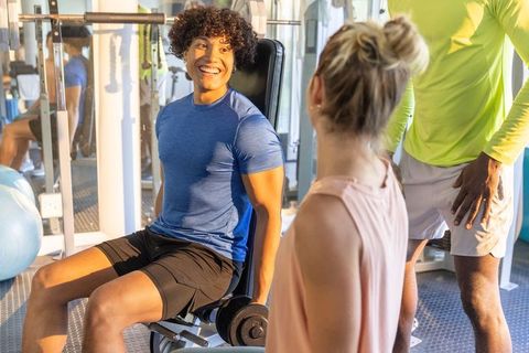 Smiling man training on weight bench with workout partners in modern gym