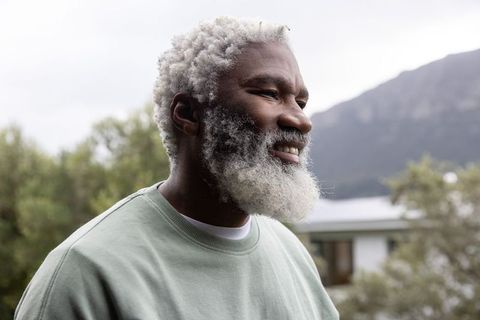 Serene African American senior man gazing at lakeside with white beard and green crewneck