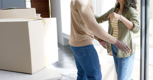 Happy biracial couple embracing with cartons at new house. Domestic life, moving house and lifestyle, unaltered.