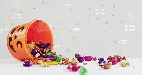 Halloween jack-o-lantern pail spilling colorful foil candies and heart sweets on white background