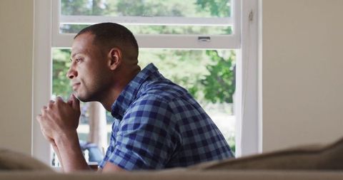 Thoughtful man looking out window, reflecting indoors