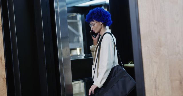 Stylish woman with striking blue hair talking on her mobile phone while at the workplace. Perfect for use in articles, advertisements, or marketing materials related to business, modern work environments, fashion trends, professional communications, or diversity in the workplace.