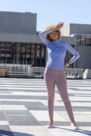 African american woman shielding eyes on urban rooftop in pastel activewear after workout