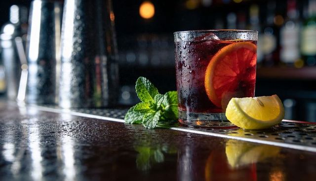 Sitting rocks glass holding moody red cocktail with lemon wedge and mint on wet bar