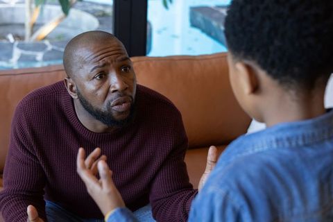African american father having serious conversation with son on couch by backyard pool