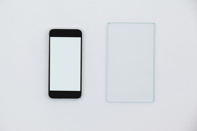 Close-up of sheet of glass and mobile phone on white background